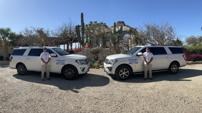 Two luxury white cars with chauffeurs standing in front of them.